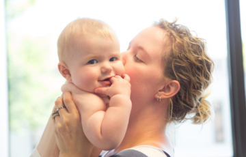 Mother holding smiling baby and kissing baby on the cheek